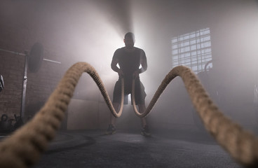 Silhouette of man working out with battle ropes at gym.
