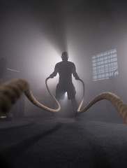 Silhouette of man working out with battle ropes at gym.