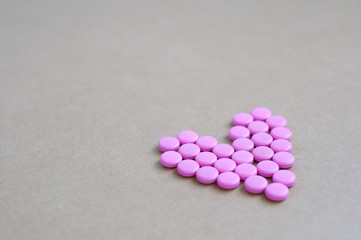 pink pills laid out in shape of a heart on brown background. coloured drugs. concept - heart disease, heart disorders and drugs, cardiology, valentines, love,