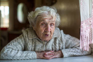 Portrait of elderly pensioner lady with an ironic look sitting at the table.
