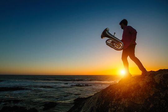 Silhouette of musician with tuba on sea shore at sunset.