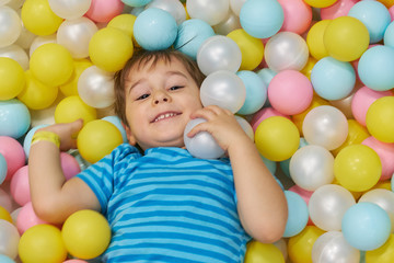 child of three years old is playing in a ball pool. boy smiling spends fun time in the nursery.