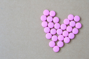 pink pills laid out in shape of a heart on brown background. coloured drugs. concept - heart disease, heart disorders and drugs, cardiology, valentines, love,