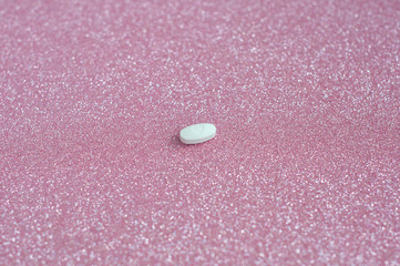 White pill with heart shape, love shape medicine isolated on glitter pink background.
