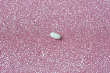 White pill with heart shape, love shape medicine isolated on glitter pink background.