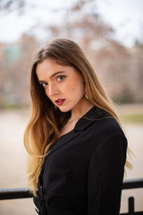 Portrait of pretty model woman posing in a park resting on a fence in autumn