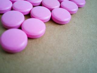Obraz na płótnie Canvas pink pills laid out in shape of a heart on brown background. coloured drugs. concept - heart disease, heart disorders and drugs, cardiology, valentines, love,