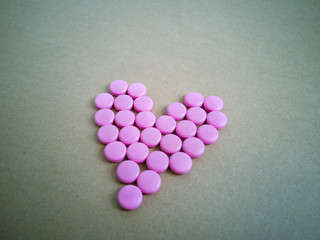 pink pills laid out in shape of a heart on brown background. coloured drugs. concept - heart disease, heart disorders and drugs, cardiology, valentines, love,