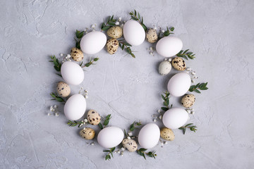 Circle border for easter card or invitation. Easter wreath with easter quail, chicken eggs and leaf sprigs of eucalyptus. On a gray concrete background with place for text.