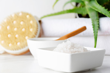 Fototapeta premium Closeup of white container with bath salt,container with clay and spoon in it, pile of white towels,green plant as background