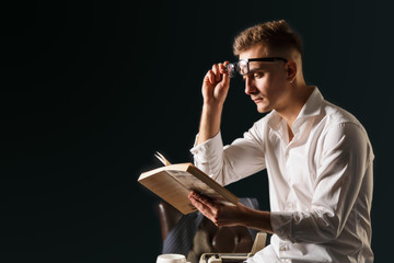 Book writer wearing glasses and white shirt sitting on the table with typewriter and reading new...