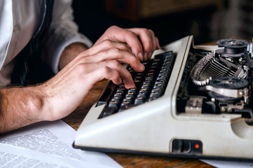 Young man's hands typing new book on an antique vintage typewriter, crop view
