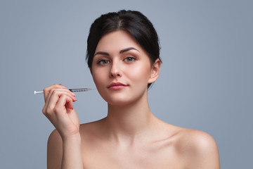 Fototapeta premium Young woman with cosmetic syringe looking at camera
