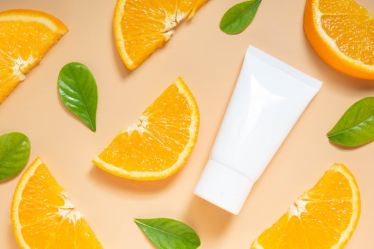 Natural vitamin c skincare products w/ fresh juicy orange fruit slice and green leaf on orange background. Cosmetic beauty product branding mock-up for moisturizing cream, lotion, foam or shampoo.