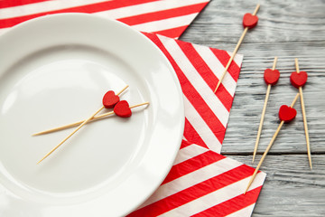 toothpicks with a small red hearts on a white plate and striped festive napkin. Close up