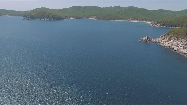 Aerial shot moving along the coastline of deep blue sea along a dramatic cliff edge on sunny day