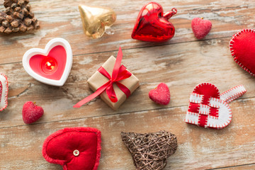 christmas, valentines day and holidays concept - gift box with heart shaped decorations and candle burning on wooden background
