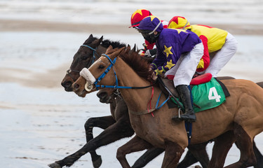 Close up action of galloping Race horses and jockeys competing on the beach