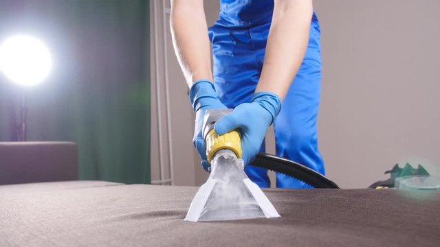 Concept of cleaning in the apartment and office. Dry cleaning worker removing dirt from sofa indoors