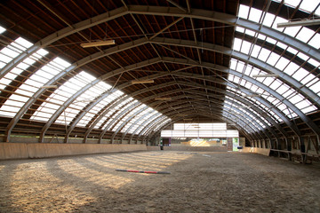 View in an empty indoor riding hall center for horses and riders. The riding school is suitable for dressage and jumping  horses