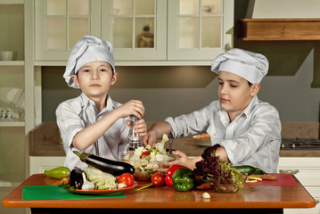 The boys in the cooks costumes cut the salad in the kitchen. Children prepare healthy food....