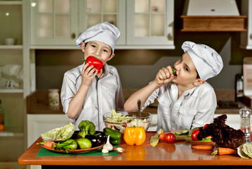 The boys in the cooks costumes cut the salad in the kitchen. Children prepare healthy food. Friendly cooperation of cooks. Eat raw vegetables.