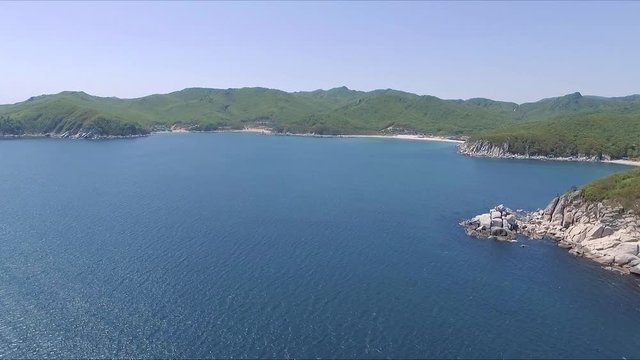 Aerial shot moving along the coastline of deep blue sea along a dramatic cliff edge on sunny day