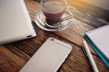 Smartphone and cup of tea on the wooden table.