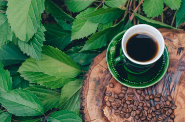 A cup of coffee on a cut tree with coffee beans and leaves.