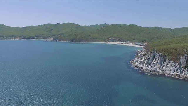 Aerial shot moving along the coastline of deep blue sea along a dramatic cliff edge on sunny day