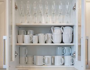 Cupboard full of white mugs and champagne glasses