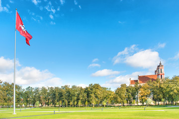 Beautiful sunny park with green grass, flying flag and old catholic cathedral in Vilnius