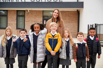 Primary school kids standing in front of school with their teacher looking to camera, front view