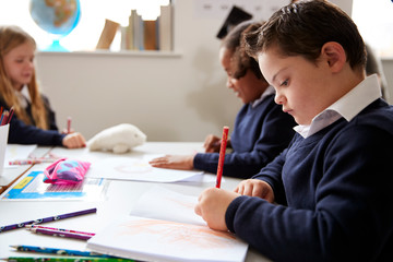 Pre-teen school boy with Down syndrome sitting at a desk writing in a primary school class, close up, side view
