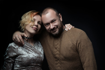 Romantic loving married couple of 30-40 years old is hugging against a dark background.