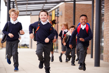Excited primary school kids, wearing school uniforms and backpacks, running on a walkway outside...