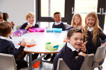 Fototapeta premium Elevated view of primary school kids sitting together at a round table to eat their packed lunches, some turning around to face the camera