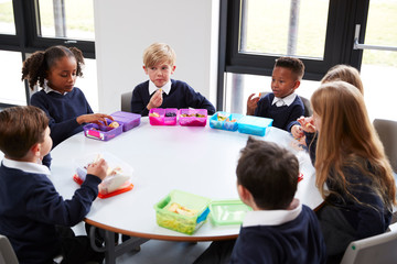 Elevated view of primary school kids sitting together at a round table eating their packed lunches