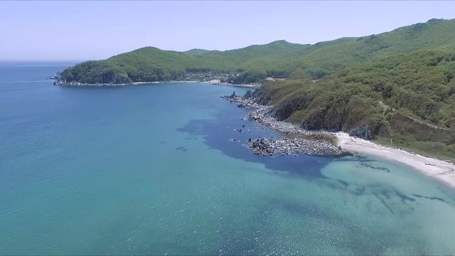 Aerial shot moving along the coastline of deep blue sea along a dramatic cliff edge on sunny day