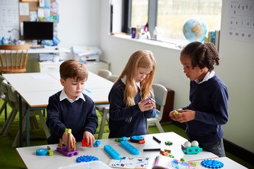 Fototapeta premium Elevated view of three primary school kids working together using construction blocks in a classroom