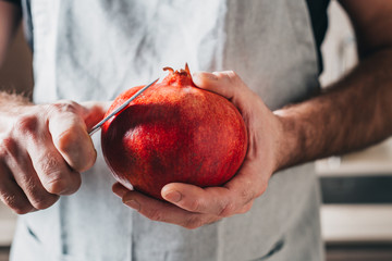 A man with strong hands cuts a pomegranate with a knife - close-up