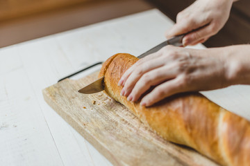 Female European hands cut fresh crisp baguette on wooden board