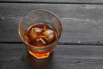 Glass of whiskey on ice with bottle on wood bar