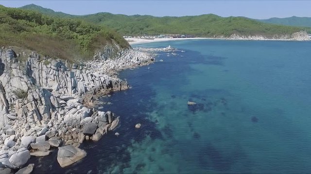Aerial shot moving along the coastline of deep blue sea along a dramatic cliff edge on sunny day