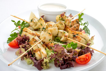 Squid grilled on skewers, with salad and sauce. On white background