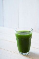 glass of green vegetable beverage on white wooden background