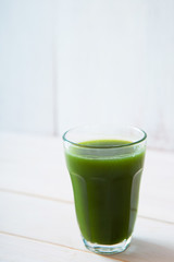 glass of green vegetable beverage on white wooden background