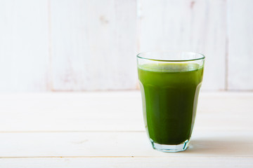 glass of green vegetable beverage on white wooden background