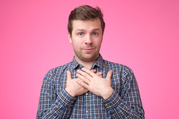 Cheerful young man smiles happily, keeps hands on chest, expresses his positive emotions.