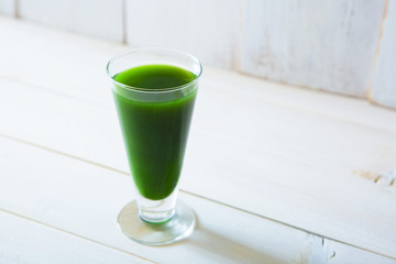 glass of green vegetable beverage on white wooden background